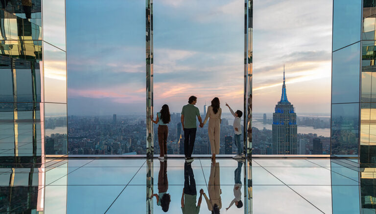 A family outing of four on a high-rise observation deck in NYC, admiring a panoramic city view at sunset.