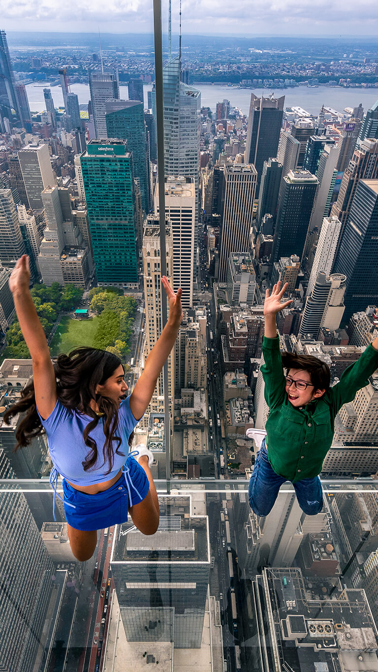 Two individuals raising their arms in joy at a New York lookout, overlooking the city skyline.