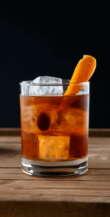 Whiskey cocktail with orange and large ice on a wooden table against a black background.